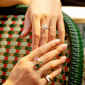 Close-up of hands wearing stacked rings with a woven chair background