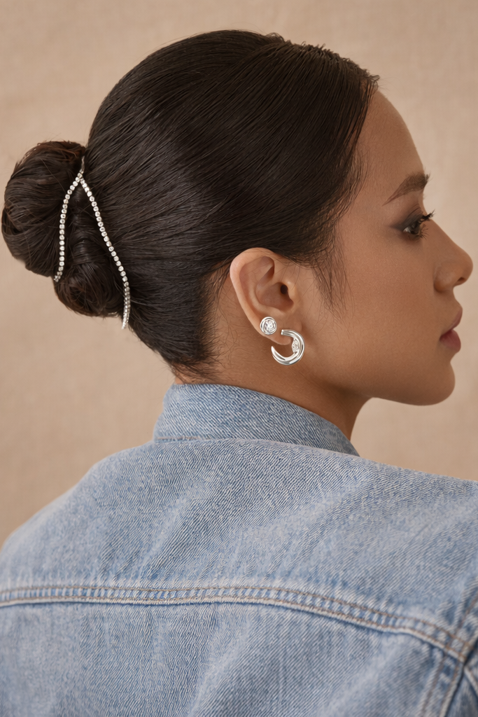 Woman with styled hair and earrings wearing a denim jacket against a beige background